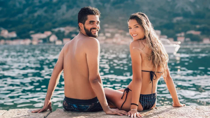 A smiling couple enjoying the sunshine by the sea with a healthy natural tan beside a promotional display for Lifegym's Sunshine In A Box natural tanning supplements. The image highlights Bora Gold and Ultra Bronze, promoting a healthy, natural-looking glow from within.